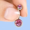 A hand holds a silver belly button piercing jewelry kit with pink gemstone studs.
