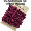 A pile of deep magenta satin hair scrunchies is shown on a cardboard background.
