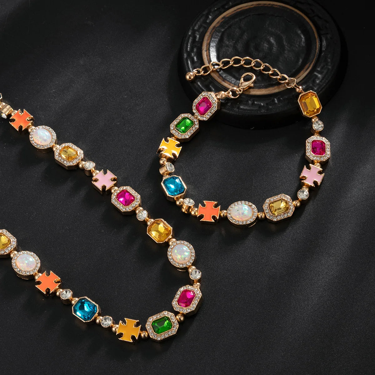 A multi-color enamel tennis chain necklace with various gemstone and enamel charms displayed on a black background.
