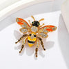 Broche dorée avec un motif d'abeille baroque et d'insecte aux accents orange, noir et jaune.