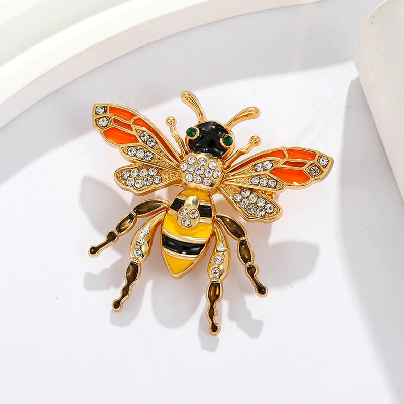 Broche dorée avec un motif d'abeille baroque et d'insecte aux accents orange, noir et jaune.
