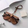 A brown PU leather pouch with a leather strap is shown next to a white box, used for eyewear storage.