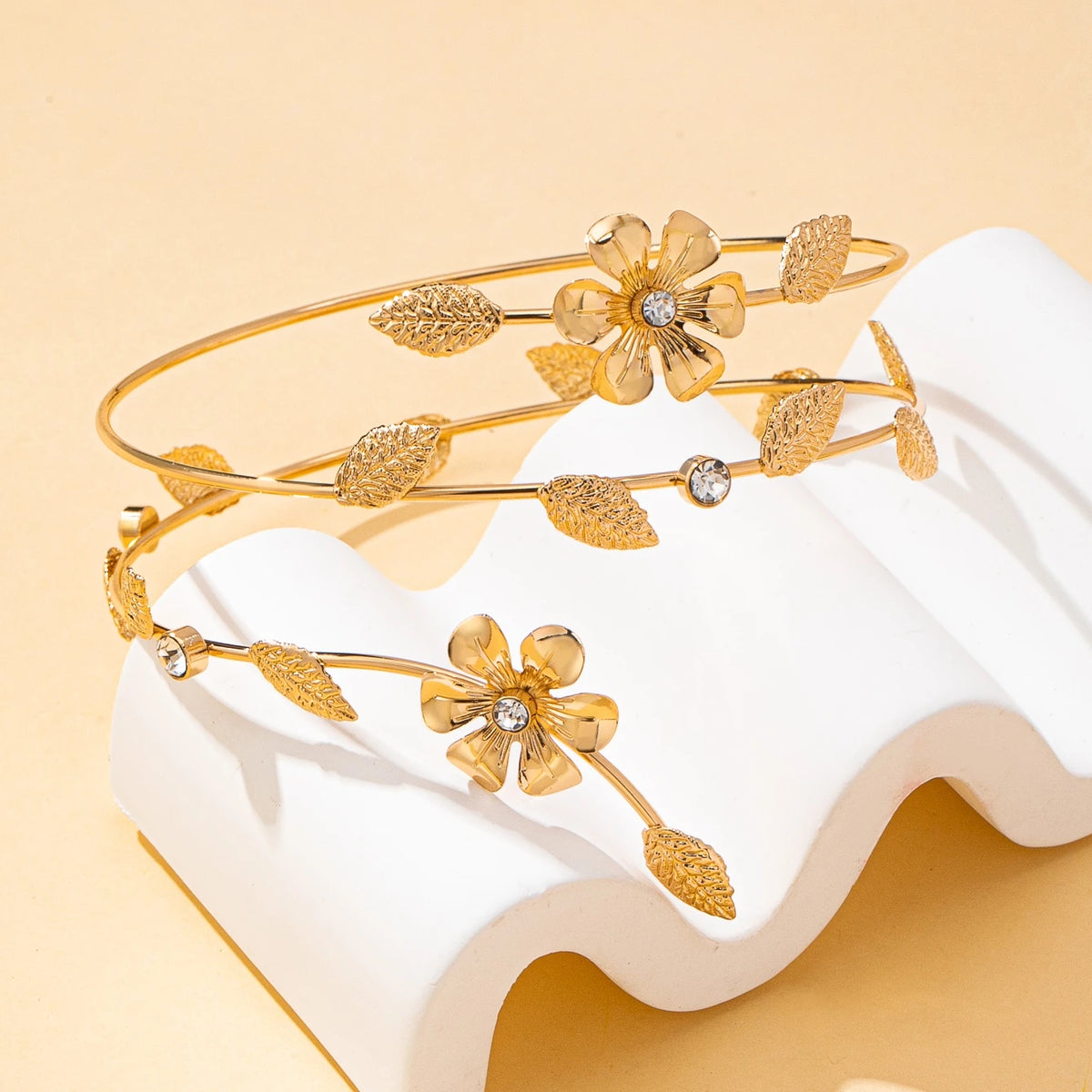 Gold floral vine arm bracelet displayed on a white ceramic stand.