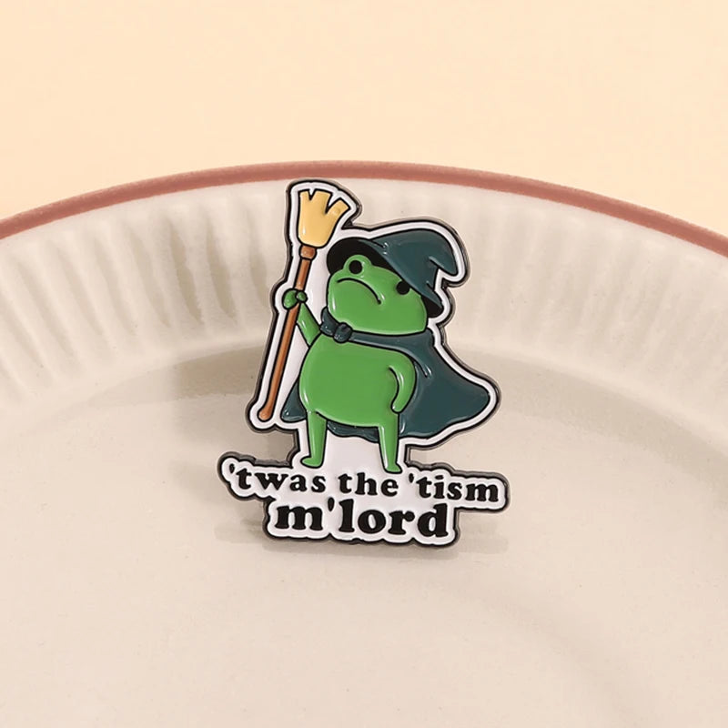 Insignia de esmalte con una rana verde usando un sombrero de mago y sosteniendo una escoba sobre un plato de cerámica rosa cl
