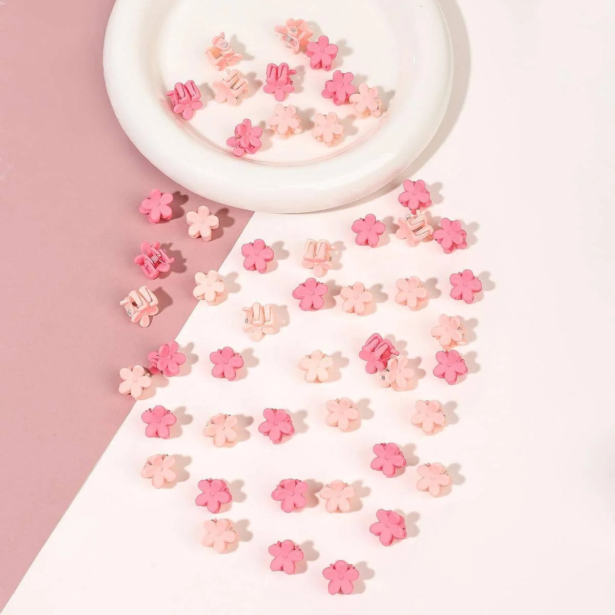 A collection of pink and coral mini flower hair clips scattered on a white surface.