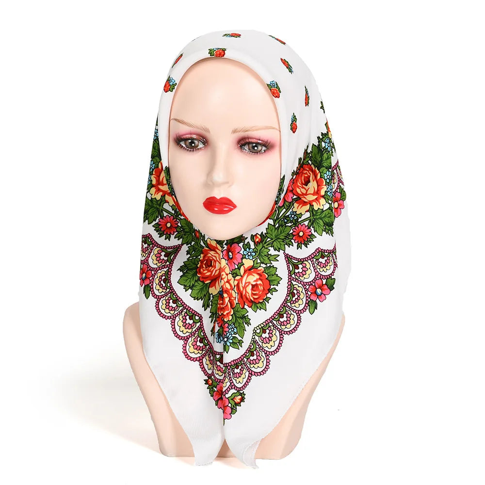 A woman wearing a white hijab with a floral print scarf featuring red, orange, and green flowers.