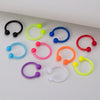 A collection of flexible acrylic piercing jewelry rings in various colors including black, lime green, blue, purple, pink, an