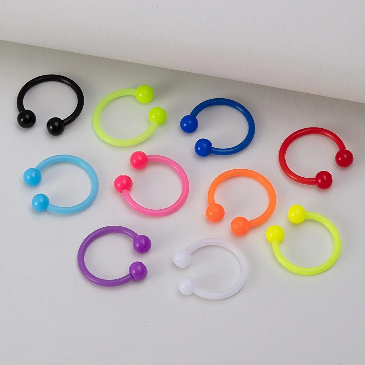 A collection of flexible acrylic piercing jewelry rings in various colors including black, lime green, blue, purple, pink, an