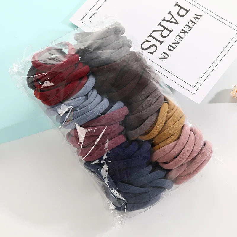 A clear plastic package containing a set of dark colored hair ropes in various shades like burgundy, gray, blue, and brown.