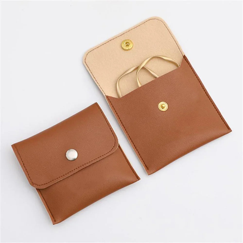 A tan leather jewelry pouch with a flap and a snap button is shown open, revealing a gold chain.