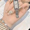 A hand wearing a silver stainless steel quartz watch with a metal bracelet and gold nail polish, resting on a document.