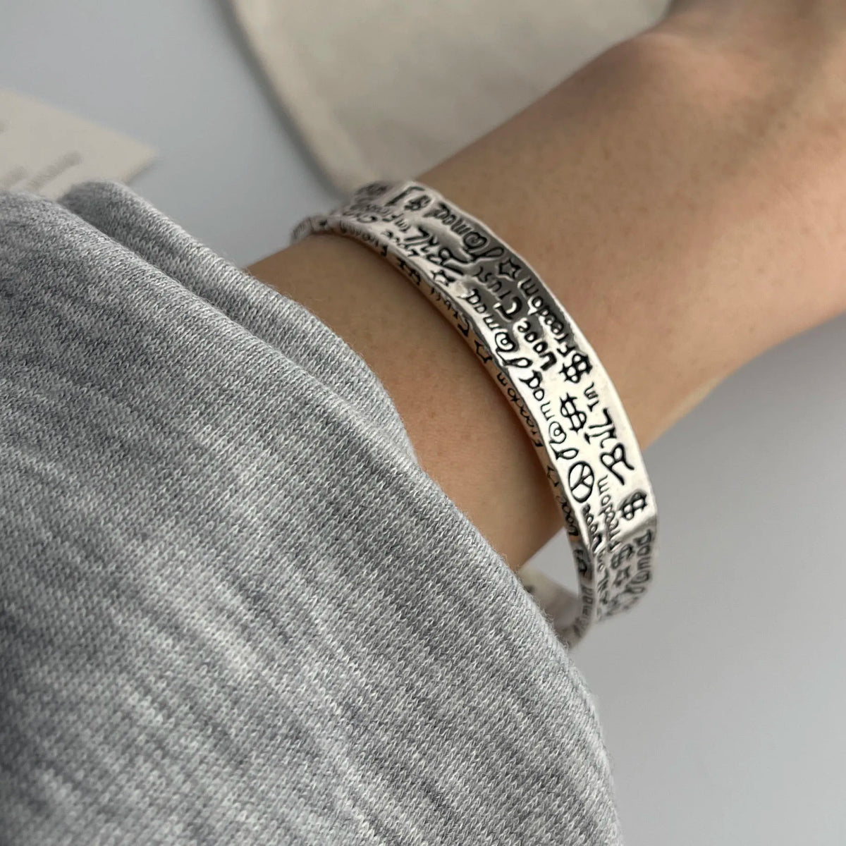 A close-up of a sterling silver charm bracelet worn on a wrist, featuring engraved charms.