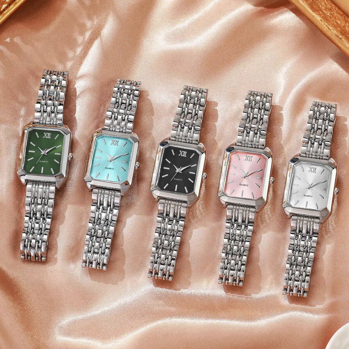 Una fila de seis elegantes relojes de pulsera de cuarzo analógicos con pulseras de metal plateado sobre un fondo de satén ros