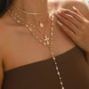 A close-up of a woman wearing a layered gold necklace featuring small pearls and a cross pendant.