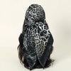 A black and gray leopard print satin silk scarf tied around dark hair.