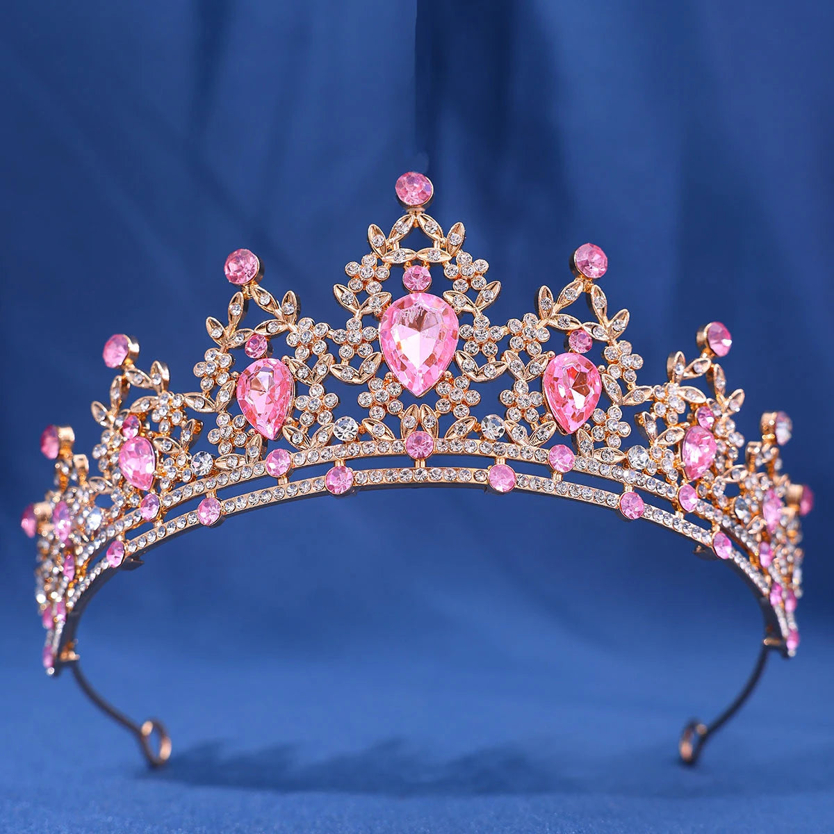 A gold crystal rhinestone tiara and headband set with pink gemstones against a blue background.