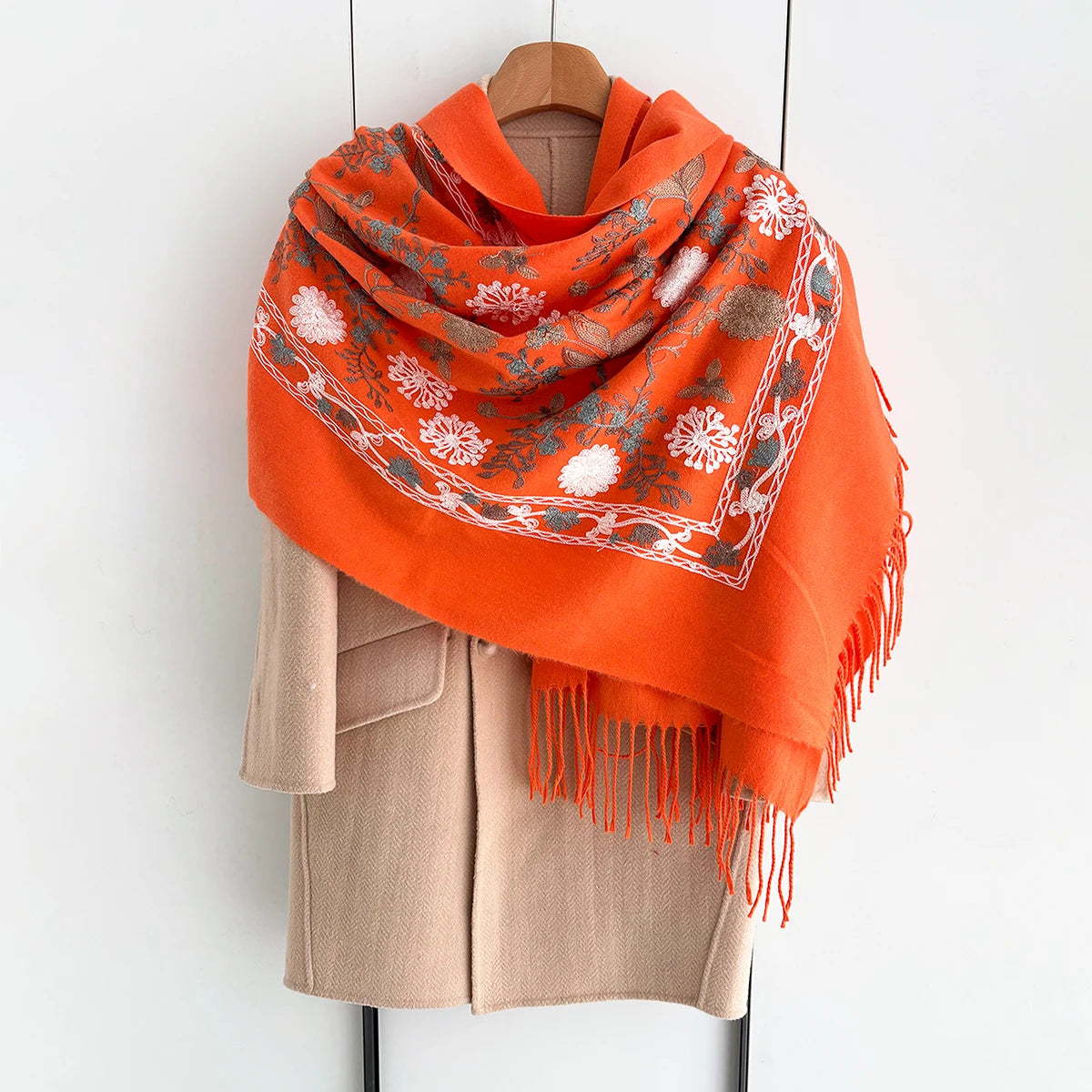 An orange luxury floral scarf draped around a beige jacket on a hanger.