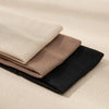 A stack of three solid color fashion headbands in beige, taupe, and black resting on a light background.