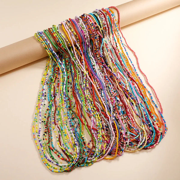 A colorful hand beaded body chain with multicolored threads draped across a light background.