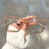 A hand holds a pair of clear square-framed glasses with rose gold accents against a light gray background.