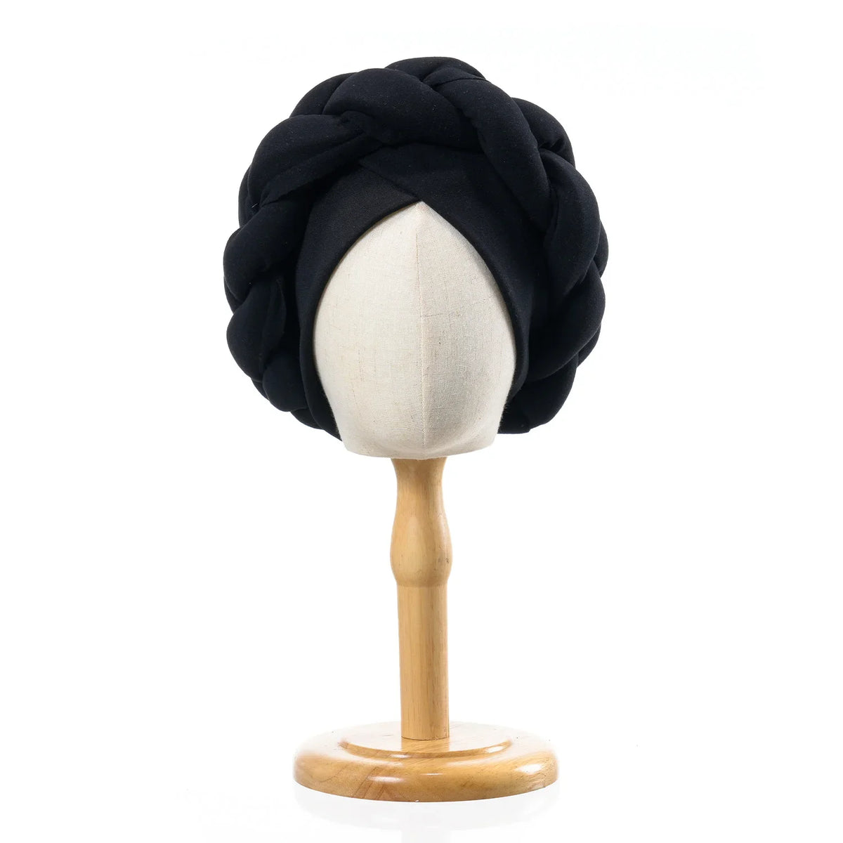 Black braided turban cap displayed on a wooden mannequin stand.