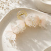 A delicate pearl rhinestone butterfly hair claw clip in a pale pink color resting on a light ceramic dish.