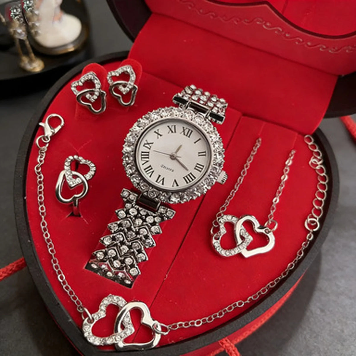 A red jewelry box containing a rhinestone heart-shaped women's jewelry set including a watch, necklace, and bracelet.