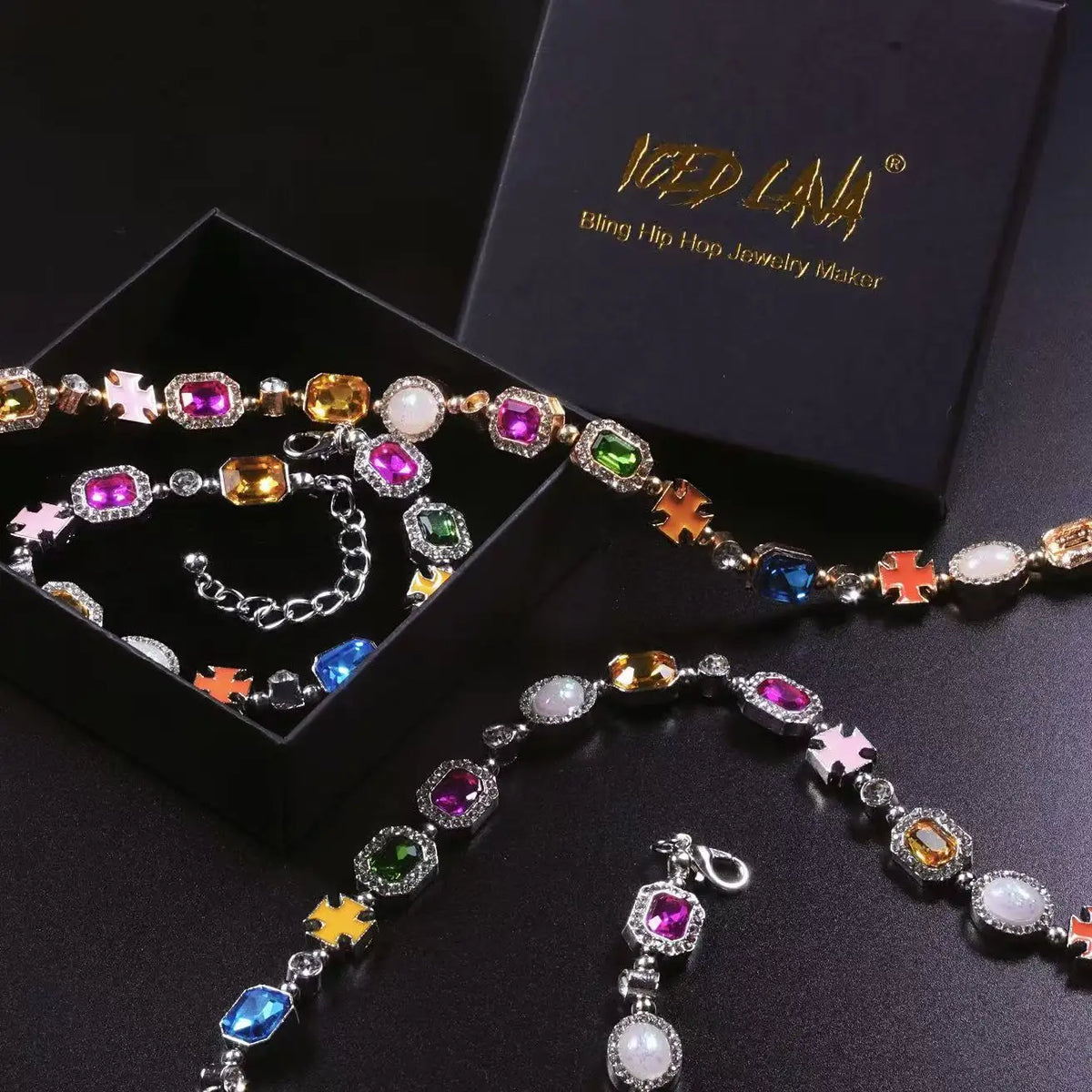 A multi-color enamel tennis chain necklace is displayed on a dark surface next to its packaging.
