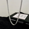 A silver stainless steel Cuban link necklace is displayed on a black surface.