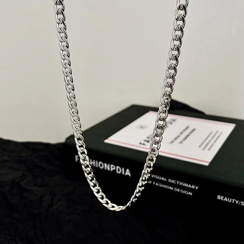A silver stainless steel Cuban link necklace is displayed on a black surface.