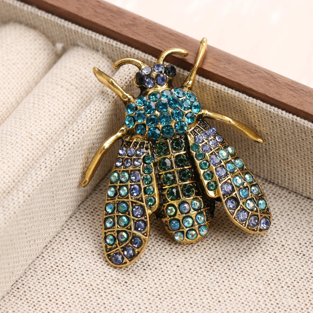 Broche baroque abeille et insecte avec métal doré et gemmes bleues, présentée dans une boîte en bois.