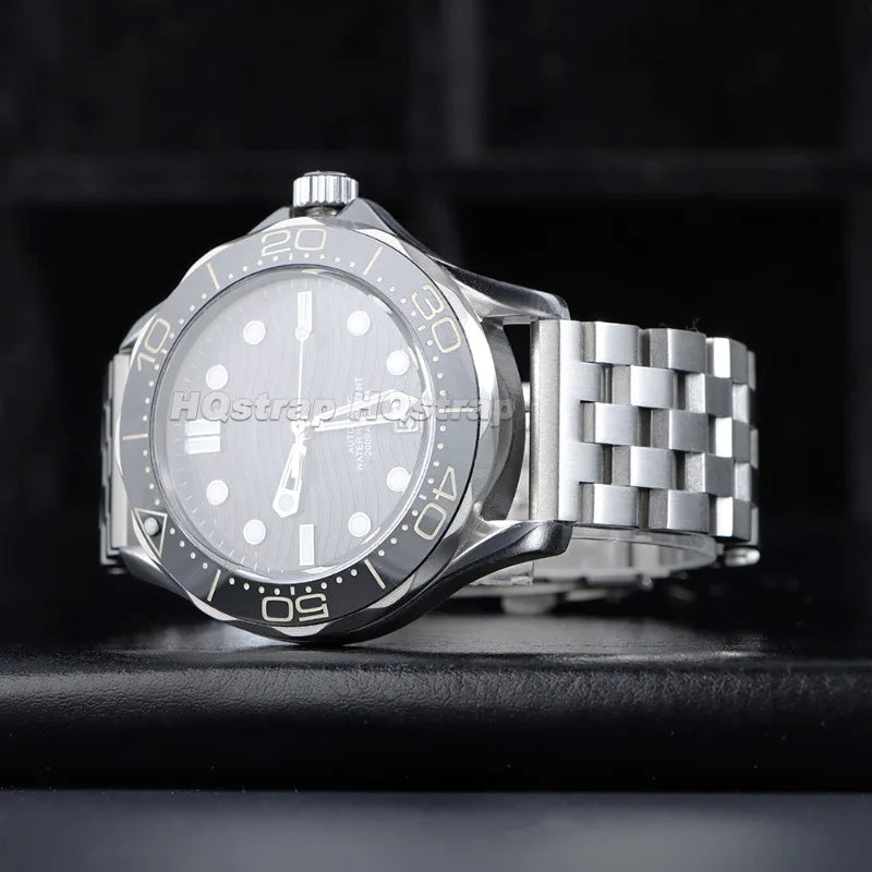 A silver stainless steel watch with a light dial and a metal link band is shown on a dark surface.