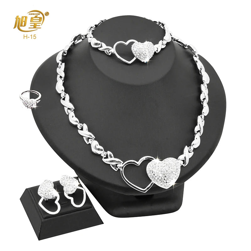A silver heart crystal necklace and matching earrings displayed on a black stand.