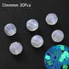 Thirty clear glow-in-the-dark acrylic beads scattered on a black surface with a close-up of blue and green light.