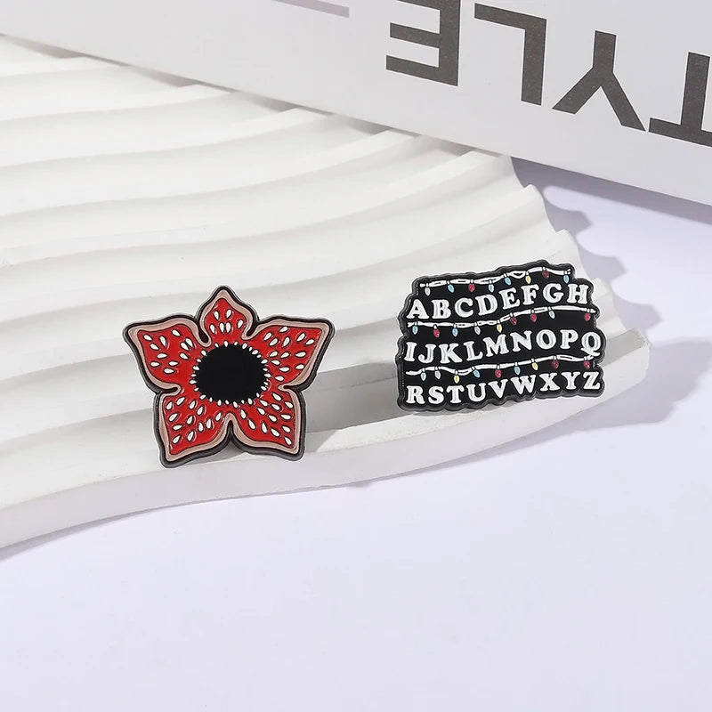 Eine Sammlung von Emaille-Pins mit einem roten Blumen- und Alphabetdesign.