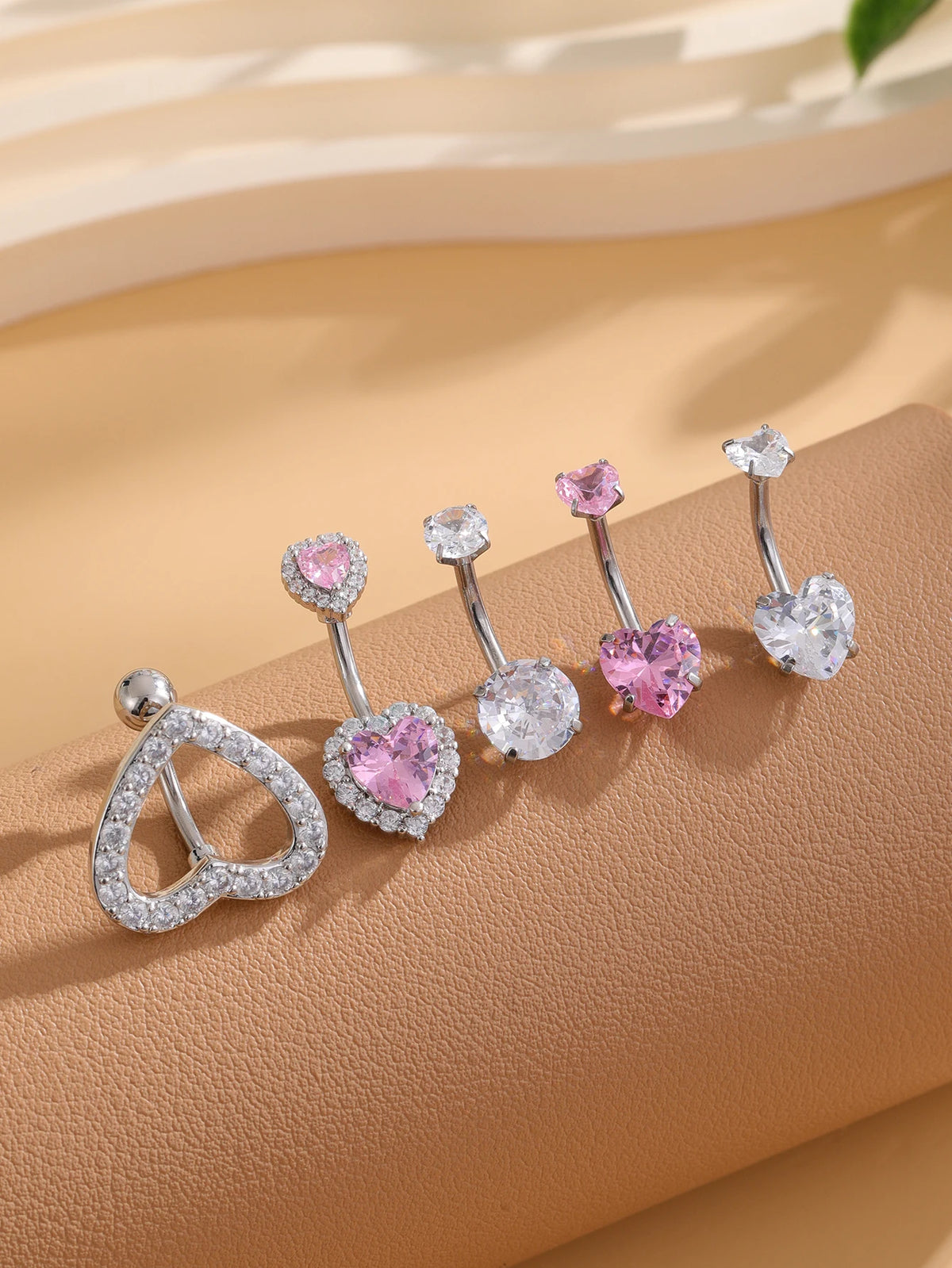 A set of five gold stainless steel dangled belly button rings featuring pink and clear gemstone designs.