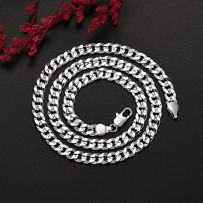 Ensemble collier et bracelet en chaîne argentée enroulé sur une surface sombre avec des feuillages rouges.