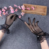 Black sheer lace fishnet evening gloves being held over pink flowers and a wooden box.
