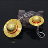 A gold and red anime style straw hat metal keychain resting on a dark stone surface.