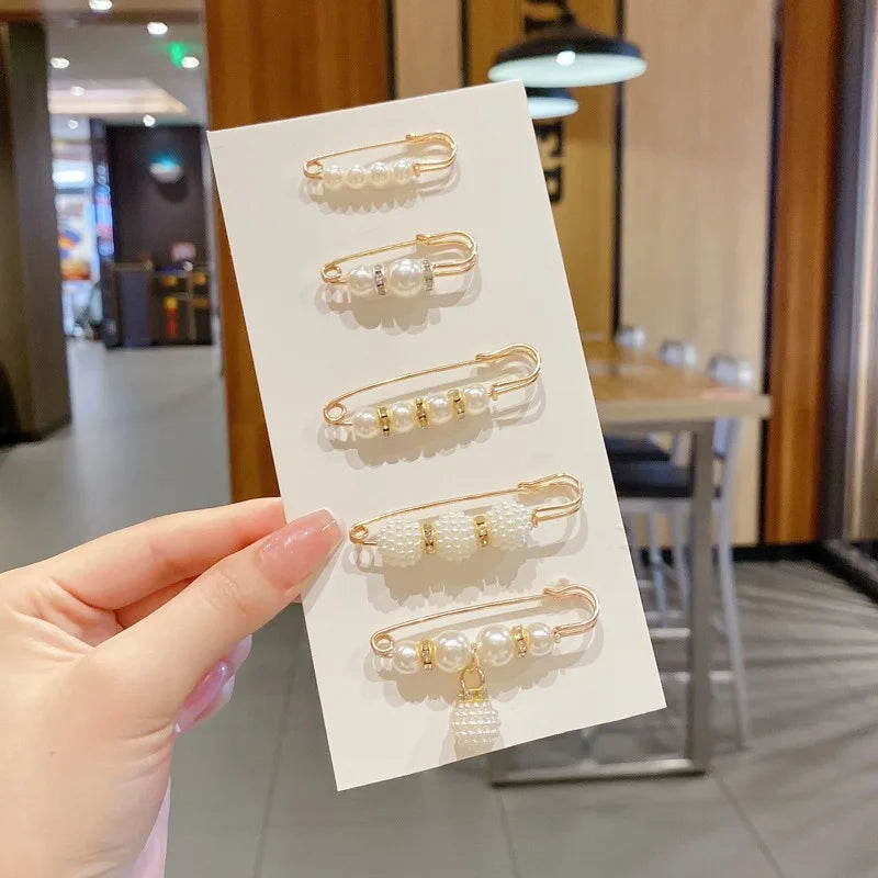 Una mano sostiene una tarjeta de exhibición con varios pines de perlas en tono dorado, dispuestos en filas.