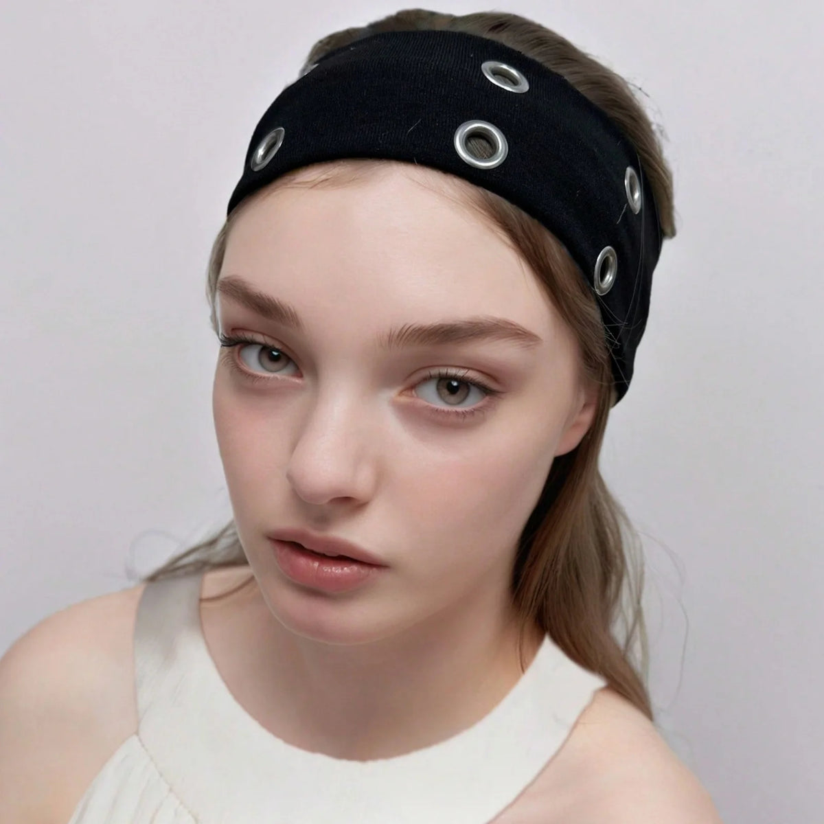 A close-up of a woman wearing a black punk style metal hollow headband with silver studs.