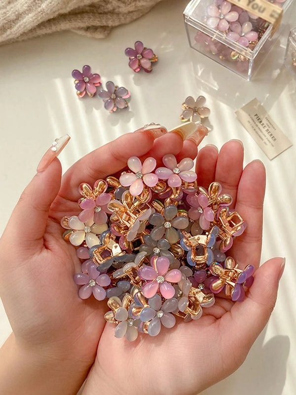 A hand holds a cluster of 10 piece super fairy flower claw hair clips in various shades of pink and purple.