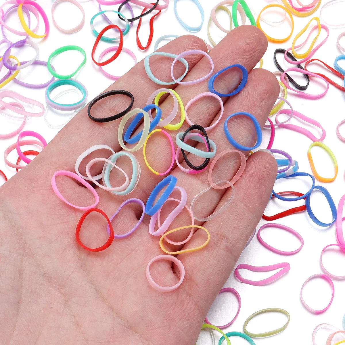 A hand holds a variety of colorful elastic hair ties in various shades including pink, yellow, blue, and black.