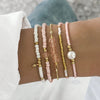 A stack of bohemian pearl beaded bracelets in white, pink, and gold on a person's wrist.