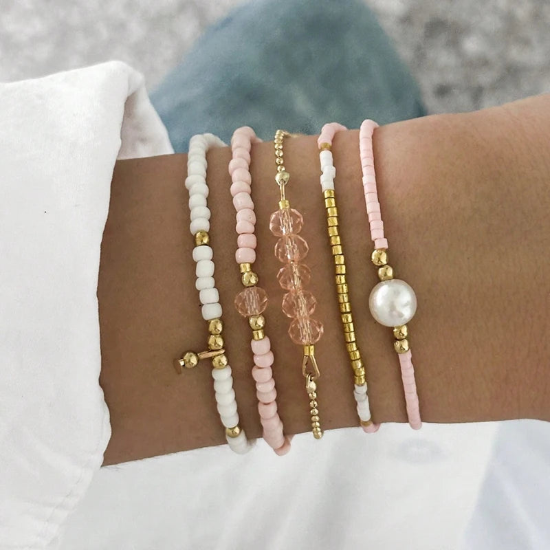 A stack of bohemian pearl beaded bracelets in white, pink, and gold on a person's wrist.
