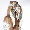 Langes blondes Haar einer Frau, gebunden mit einem gemusterten Seideschal als Boho-Halstuch.