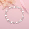 A silver heart charm bracelet made of 925 sterling silver, displayed on a pink background.