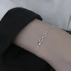 A close-up of a sterling silver double heart charm bracelet worn on a wrist against a dark sleeve.