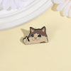 A cute enamel pin of a cat with teary eyes and a happy expression resting on a light yellow background.