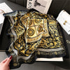 A black and gold patterned silk scarf or square shawl with intricate baroque and geometric designs.
